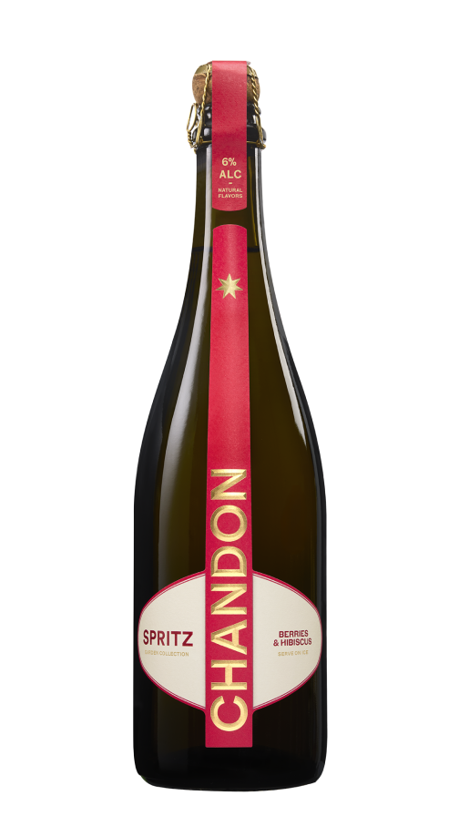 Eine Flasche Chandon Spritz Berries & Hibiscus neben einem Glas Chandon Spritz garniert mit frischen Himbeeren und einem Minzblatt, vor dem Hintergrund einer sonnigen Stadtlandschaft und unter blauem Himmel.