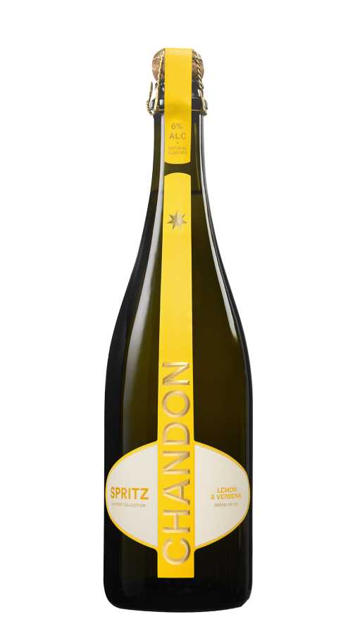 Eine Flasche Chandon Spritz Lemon & Verbena neben einem Glas Chandon Spritz Cocktail, garniert mit einer Zitronenscheibe und einem Rosmarinzweig, vor einem sonnigen Stadtbildhintergrund.