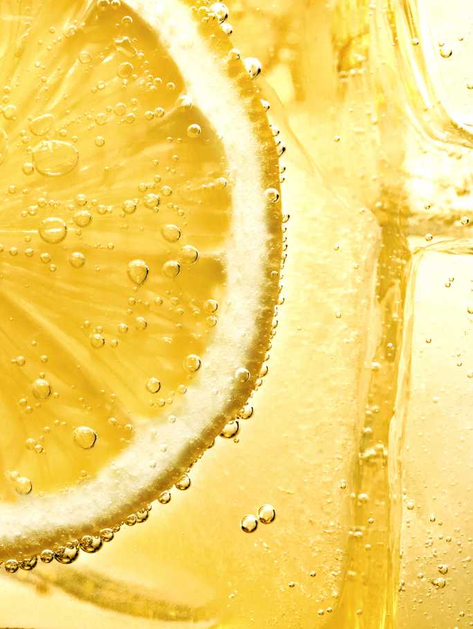 Nahaufnahme einer Zitronenscheibe, die in einer sprudelnden, gelben Flüssigkeit eingetaucht ist.