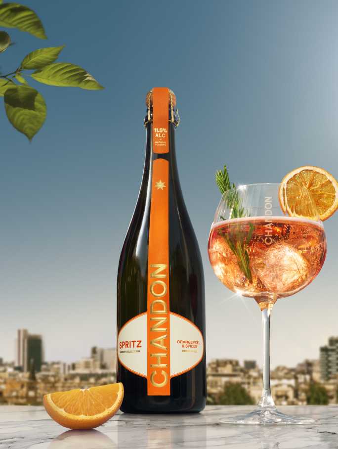 Chandon Spritz bottle and a glass of Chandon Spritz cocktail garnished with an orange slice and rosemary, set against a sunny cityscape background.