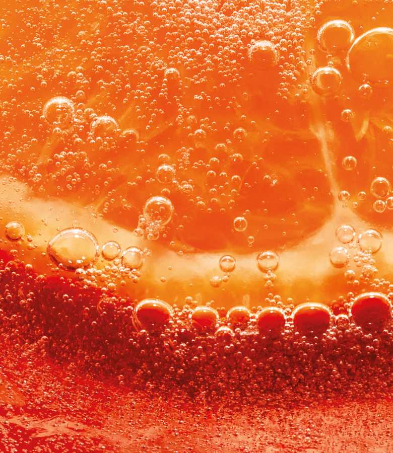 Gros plan d'une tranche d'orange immergée dans un liquide pétillant, de couleur orangée