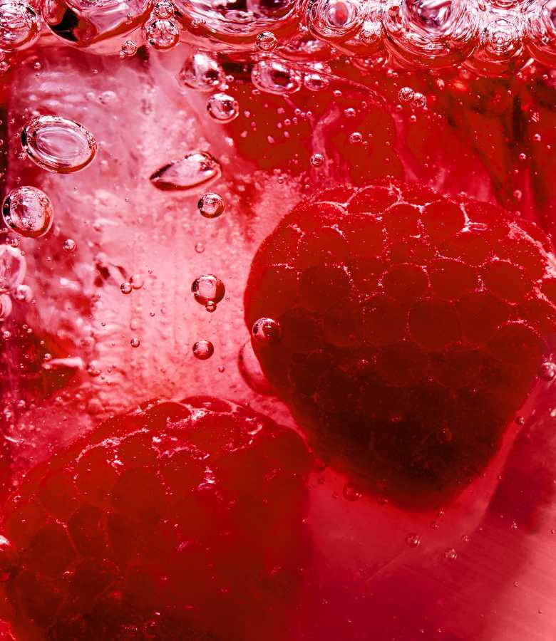 Gros plan sur deux framboises fraîches immergées dans un liquide rouge pétillant.