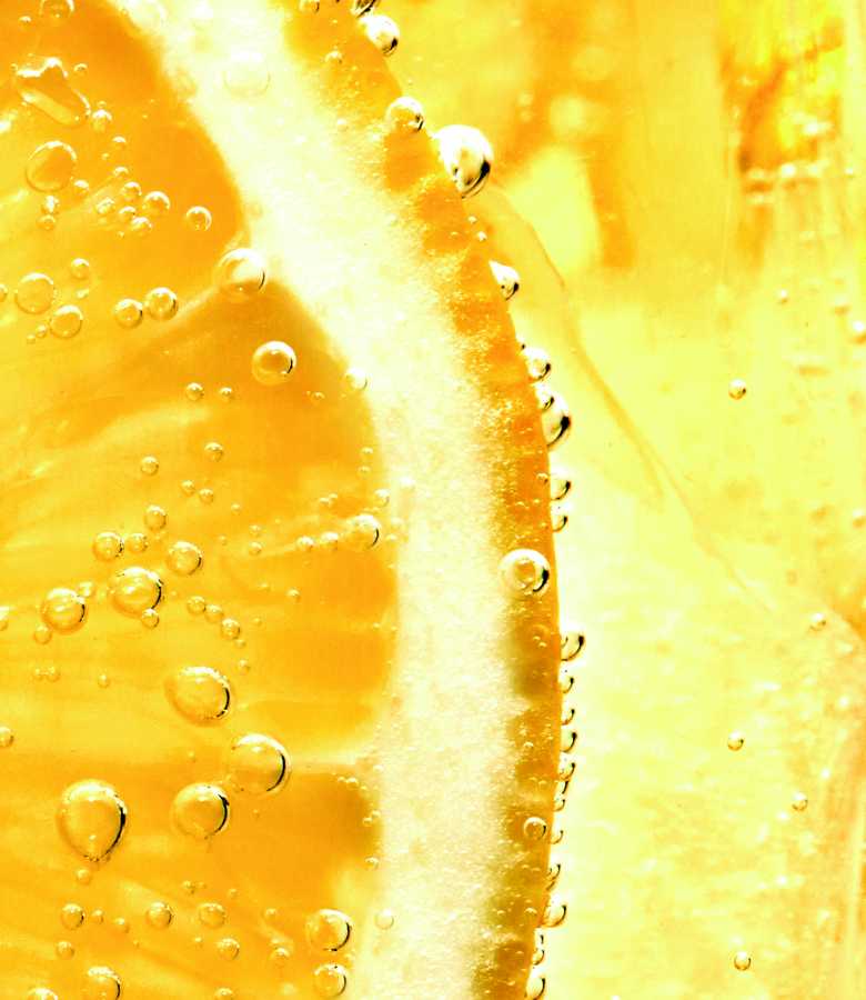 Gros plan d'une tranche de citron immergée dans un liquide pétillant, de couleur jaune