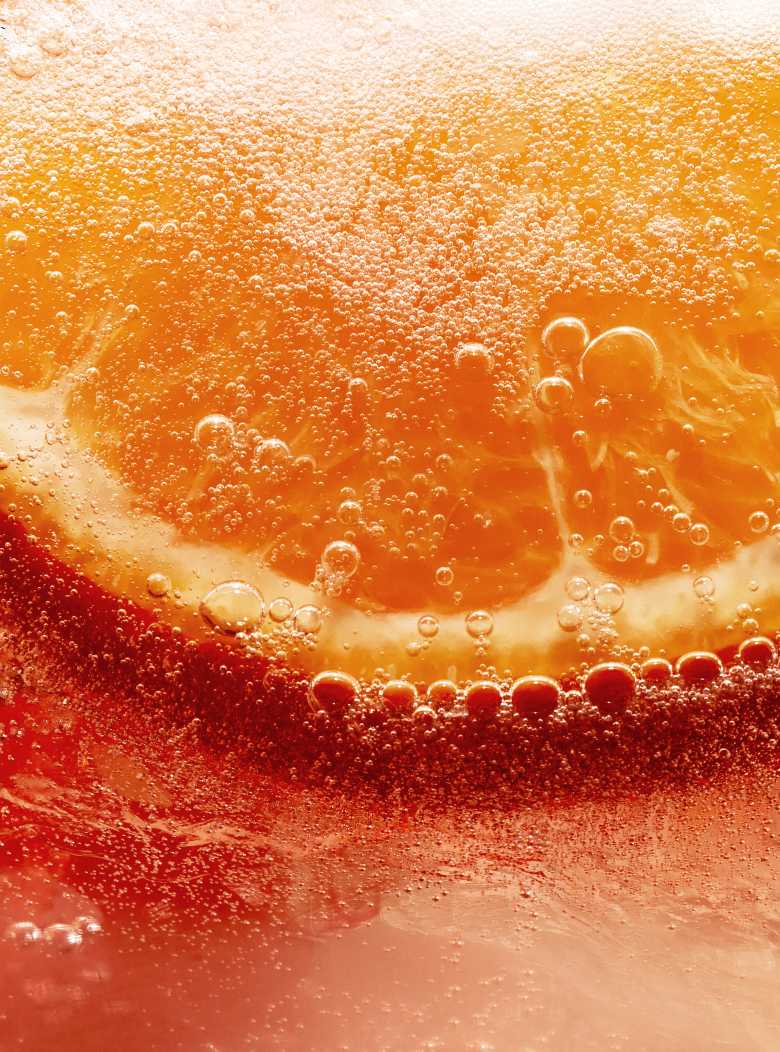 Close-up of an orange slice submerged in a bubbly, orange-hued liquid.