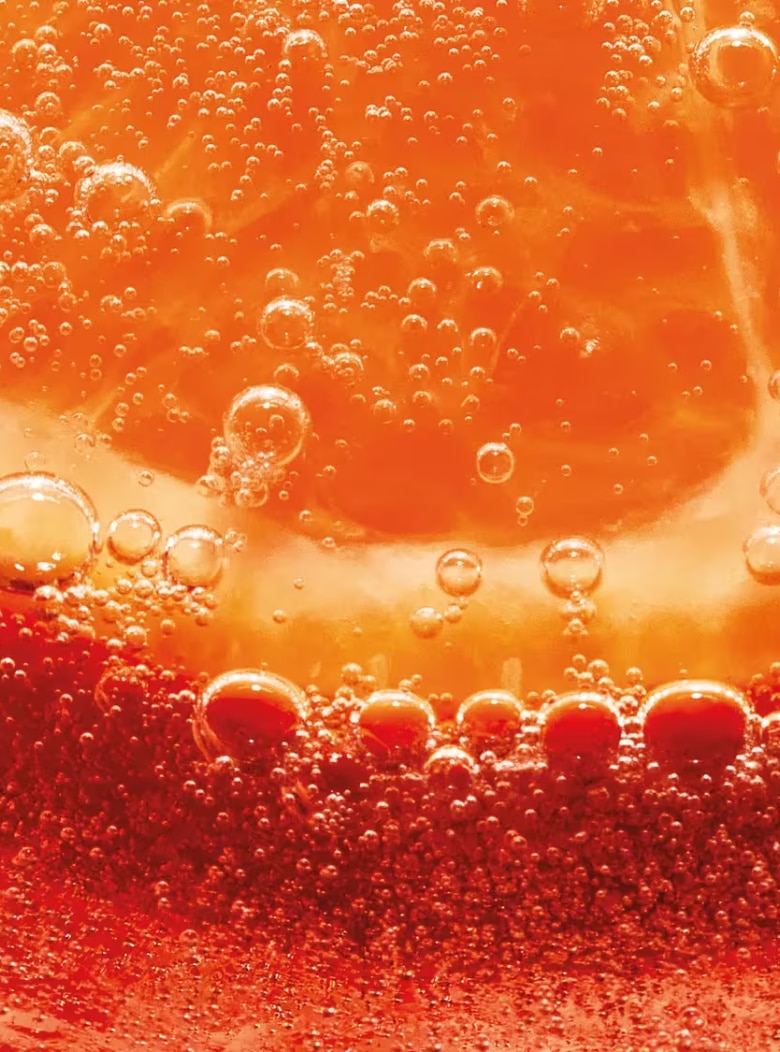 Close-up of an orange slice submerged in a bubbly, orange-hued liquid.