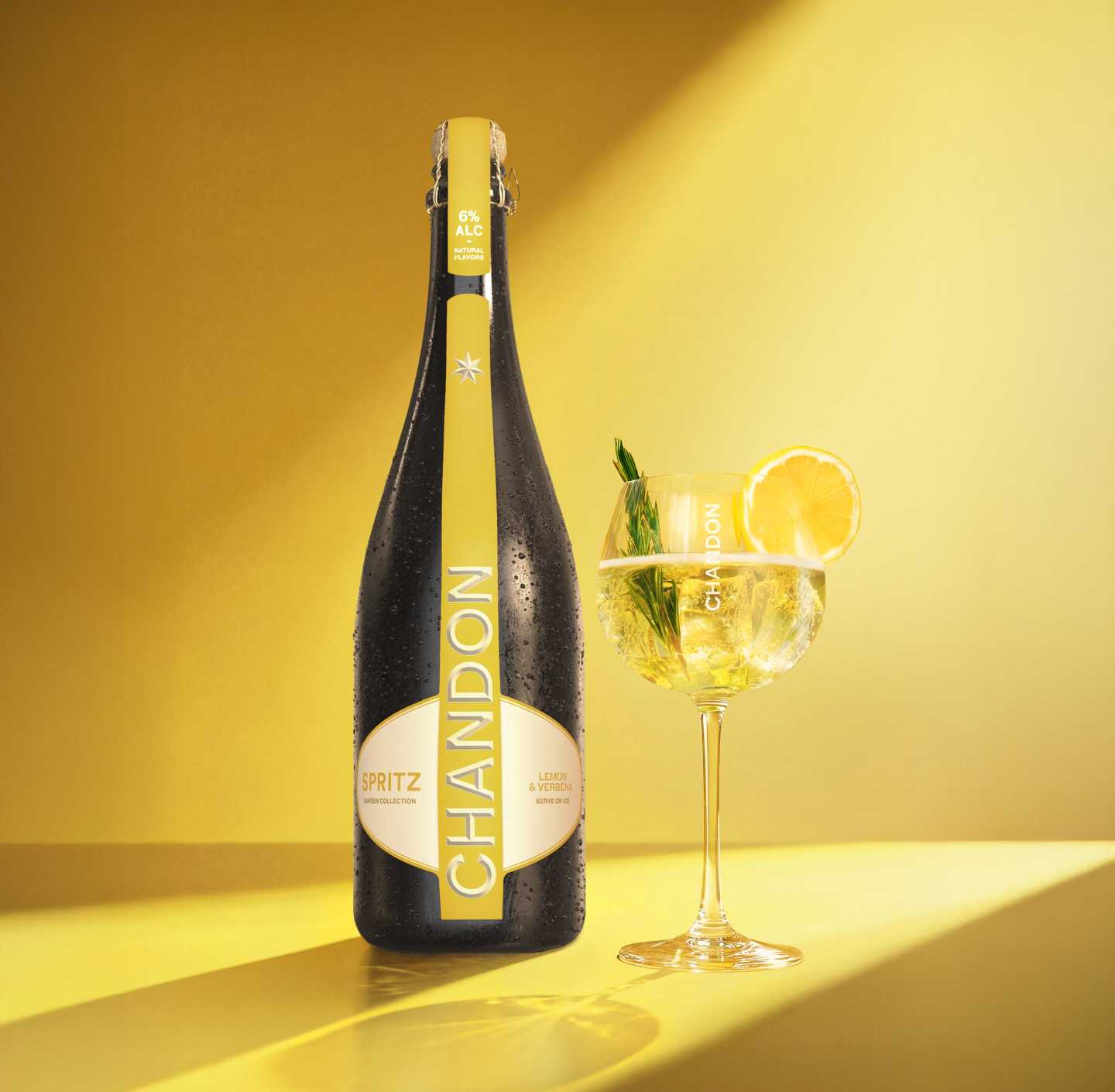 Une bouteille de Chandon Spritz Lemon & Verbena à côté d'un verre de cocktail Chandon Spritz garni d'une tranche de citron et d'un brin de romarin.