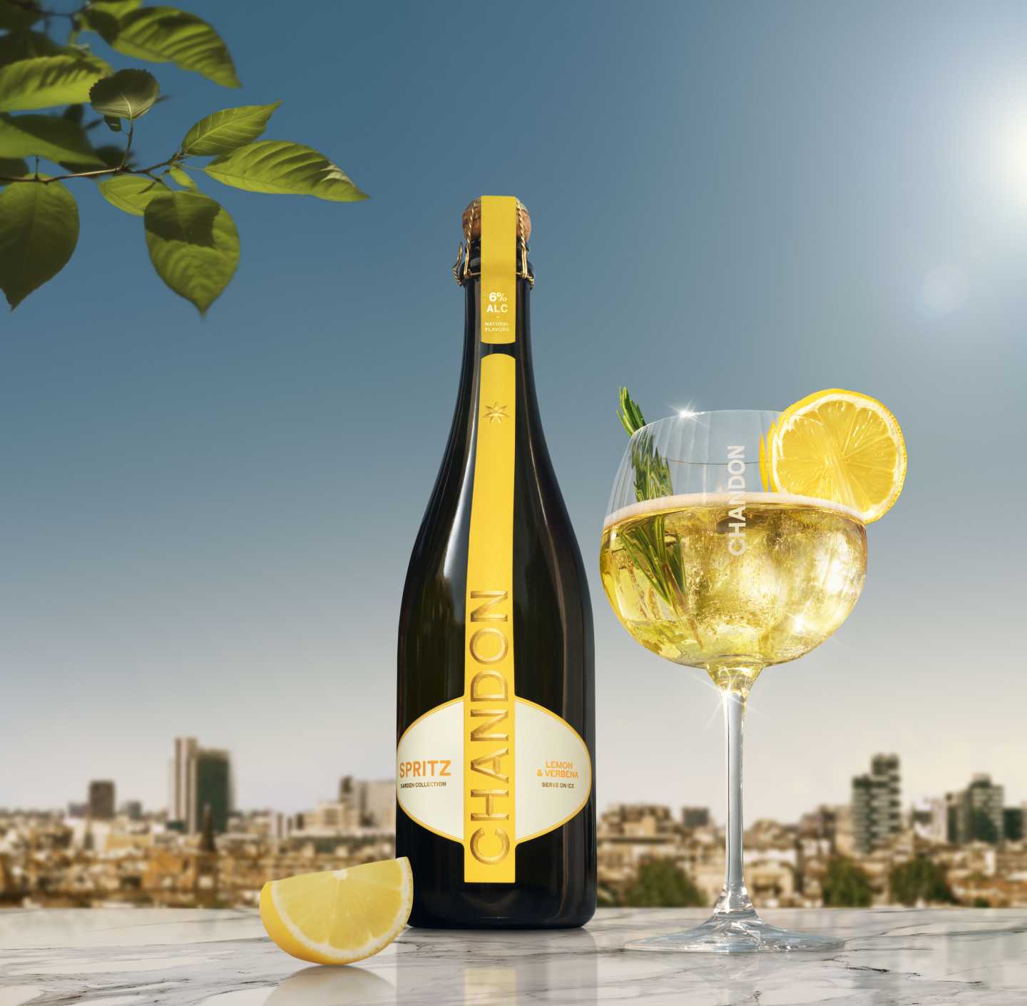 Eine Flasche Chandon Spritz Lemon & Verbena neben einem Glas Chandon Spritz Cocktail, garniert mit einer Zitronenscheibe und einem Rosmarinzweig, vor einem sonnigen Stadtbildhintergrund.