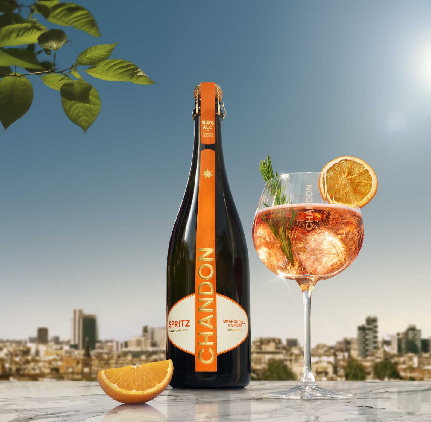 Chandon Spritz Flasche und ein Glas Chandon Spritz, garniert mit einer Orangenscheibe und Rosmarin, vor dem Hintergrund einer sonnigen Stadtlandschaft.