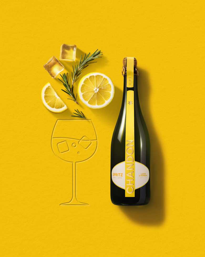 Eine Flasche Chandon Spritz Lemon & Verbena neben der Skizze eines Weinglases, mit Eiswürfeln, einer Zitronenscheibe und einem Rosmarinzweig auf einem leuchtend gelben Hintergrund.