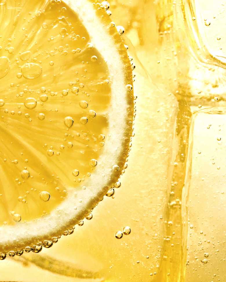 Close-up of a lemon slice submerged in a bubbly, yellow liquid.